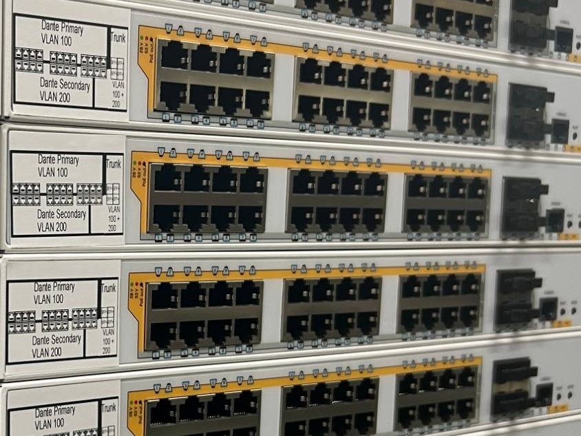 Switches mit Etiketten zur Portbelegung: Dante Primary VLAN 100, Dante Secondary VLAN 200 und Trunk