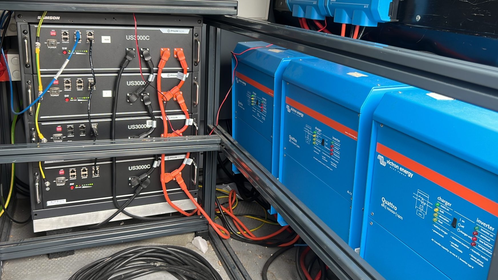 Akkuspeicher aus vier Batteriemodulen neben drei Wechselrichtern in einem Geräteregal
