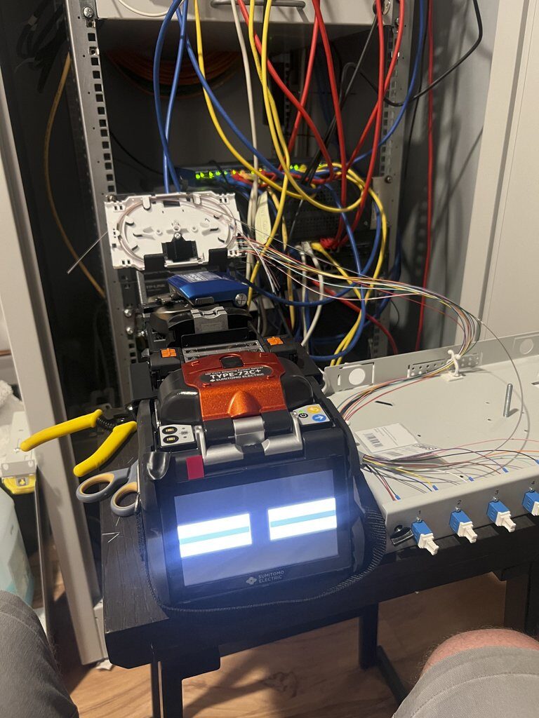 Glasfaser-Spleißgerät vor einem geöffneten Netzwerkschrank mit Patchkabeln